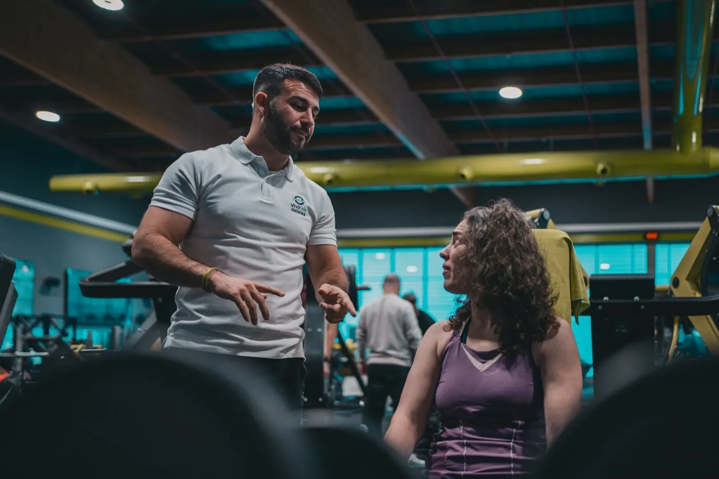 Un coach explique un exercice à une athlète assise dans une salle de sport.